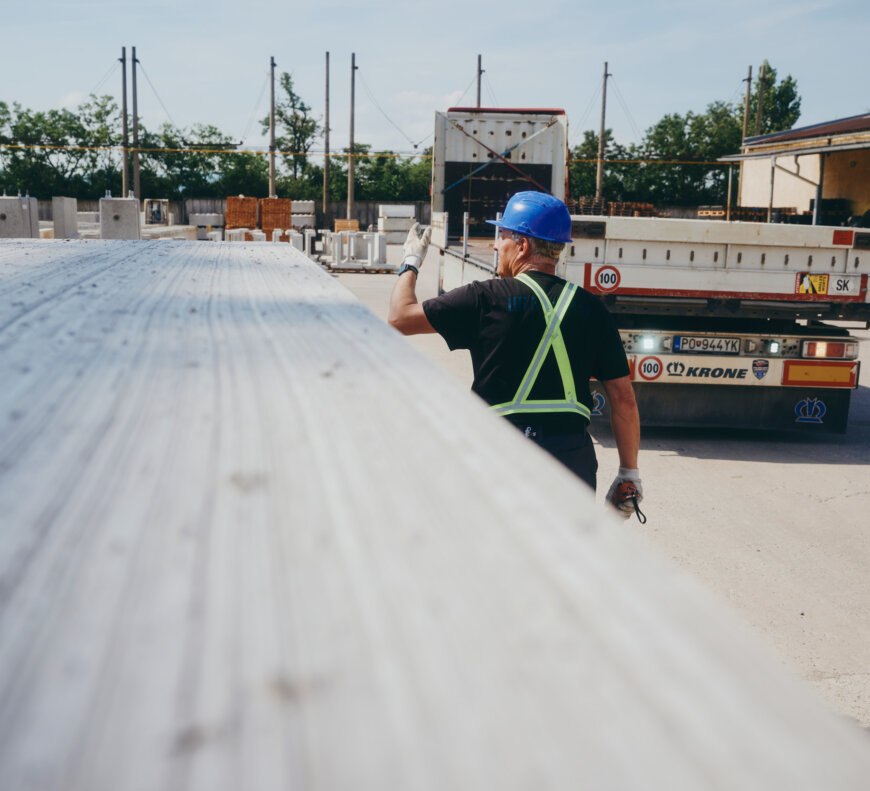 moll-rail-slowakia-worker-in-blue-hardhat-gesturing-near-flatbed-trailer-next-to-concrete-slabs moll-rail-slowakia-worker-in-blue-hardhat-gesturing-near-flatbed-trailer-next-to-concrete-slabs