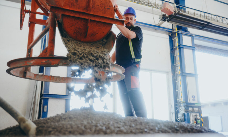 moll-rail-slowakia-worker-in-blue-hardhat-pouring-concrete-from-orange-hopper-in-factory